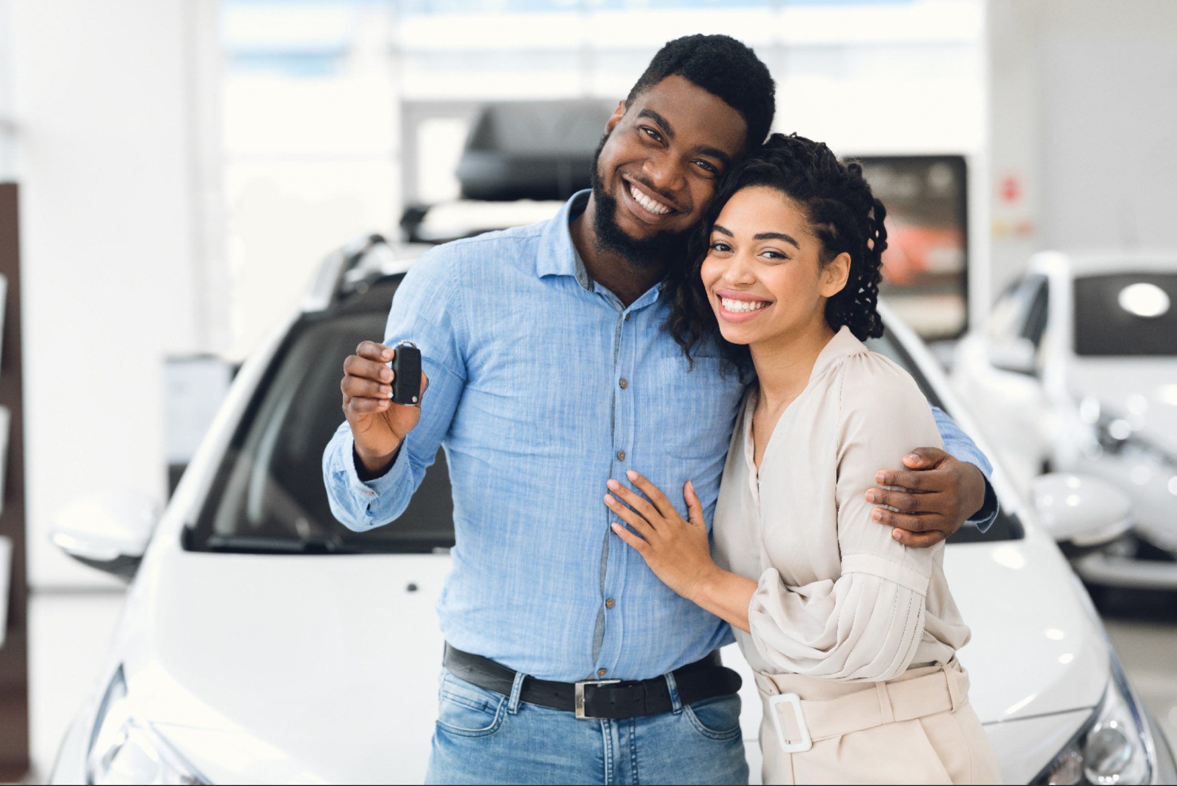 Um homem e uma mulher felizes seguram chaves, posando ao lado de um carro em uma concessionária.