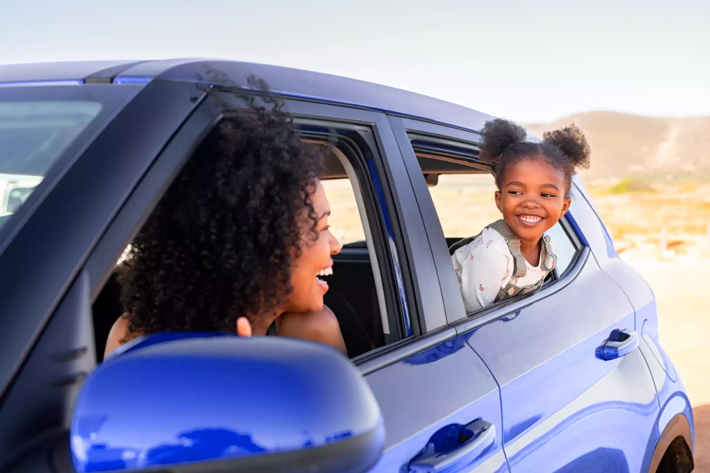 Uma mulher e uma criança sorrindo e observando a paisagem pela janela de um carro.