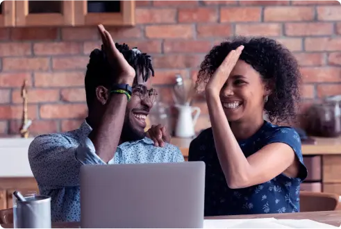 Homem e mulher sentados atrás de um computador em um ambiente com paredes de tijolos, sorrindo e batendo as mãos.