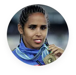 Ex-ginasta Ádria Santos, sorrindo, com uniforme azul e segurando para a câmera uma medalha de ouro pendurada em seu peito.