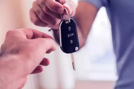 Mão de uma pessoa passando a chave de um carro para outra pessoa.