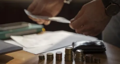 Pessoa organizando papéis de alienação fiduciária de veículo e em cima de uma mesa encontra-se uma pilha de moedas e uma carteira.