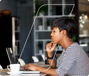 Mulher olhando para a tela de um computador portátil, sentada em uma mesa de trabalho e tocando o teclado