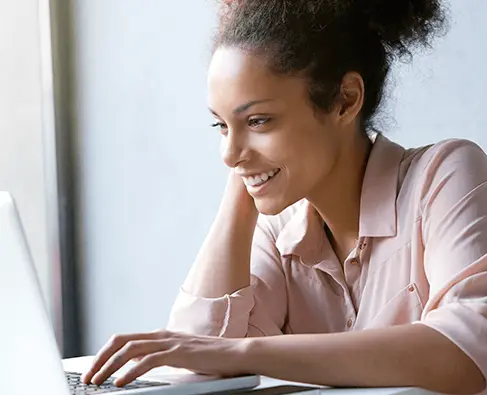 Mulher sorrindo, sentada e olhando para a tela de um computador portátil