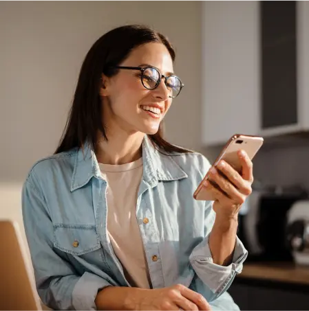 Na imagem há uma mulher de cabelos longos e escuros segurando um celular sorrindo.