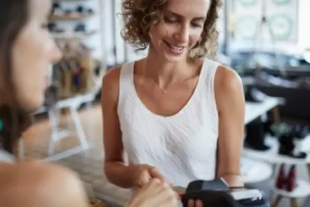 Na imagem é possível observar uma mulher sorrindo ao pagar uma conta com o cartão de crédito.