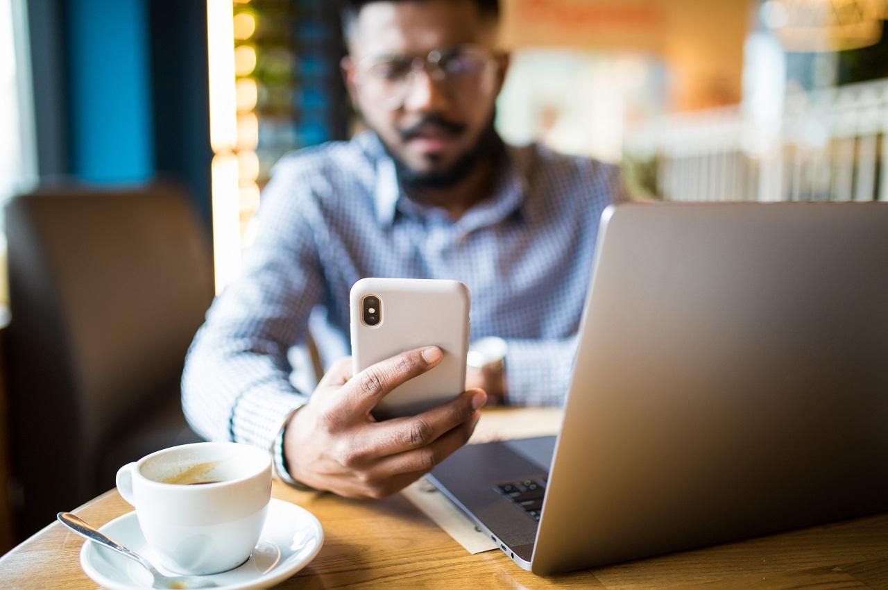 Homem com expressão concentrada e desfocado na imagem. Ele usa celular para pesquisar vantagens do empréstimo consignado.