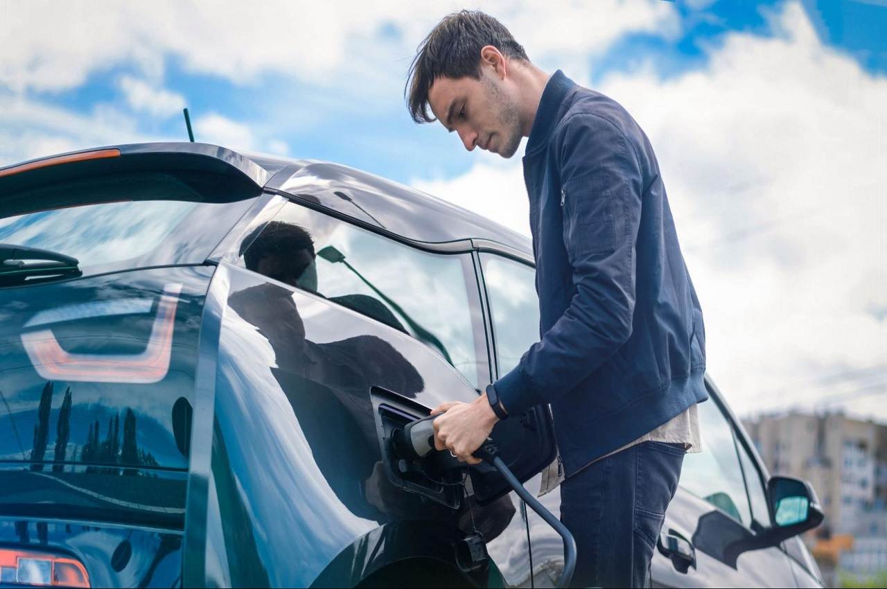 Homem recarregando seu carro elétrico com uma mangueira de energia.