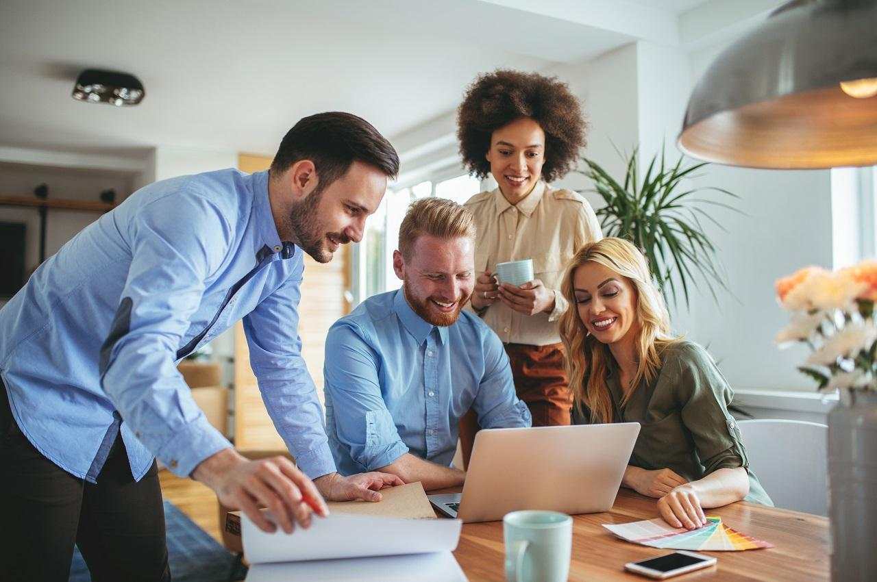 A imagem mostra um grupo de pessoas sorridentes trabalhando em um escritório.