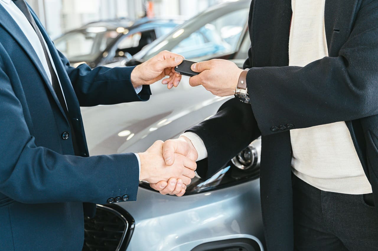 Um homem entregando as chaves de um carro a outro homem, com um aperto de mão em celebração a troca de carro financiado.