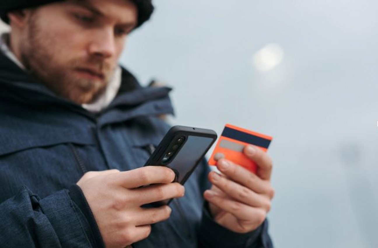 O texto mostra um rapaz fazendo comprar com seu cartão de crédito pelo celular.