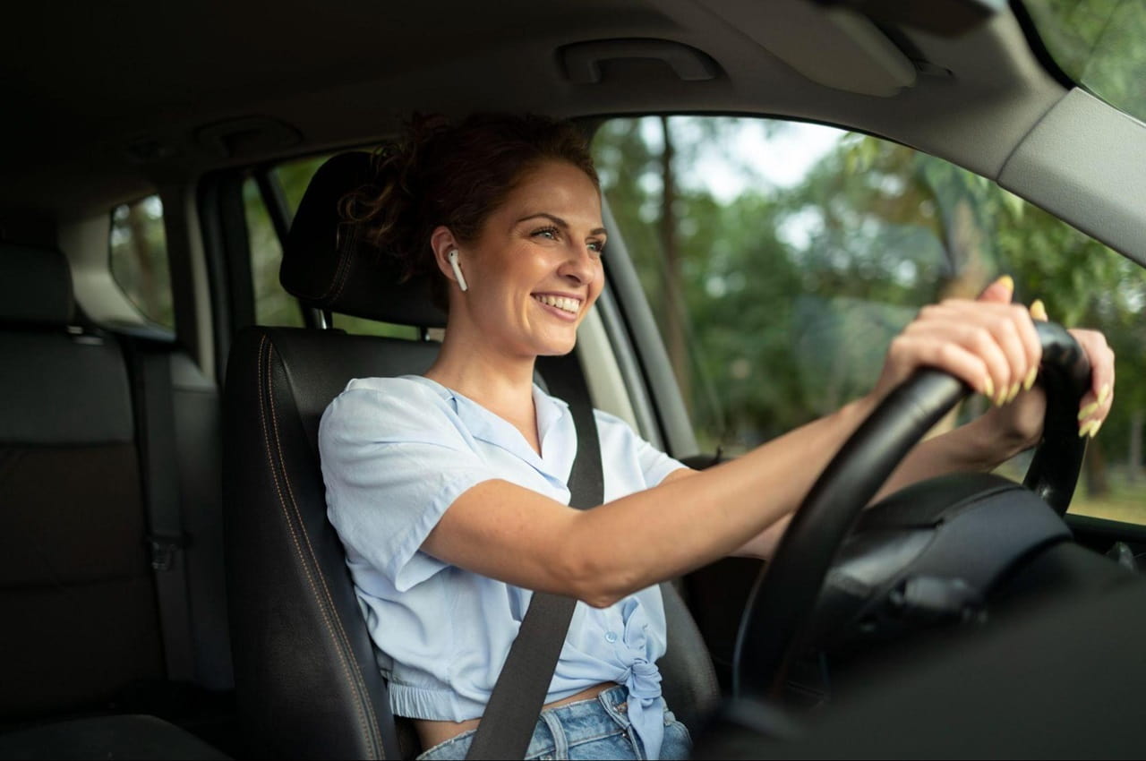 Mulher sorridente dirige um carro com IPVA pago. Ela veste blusa de babados azul-clara e tem cabelos castanhos presos.