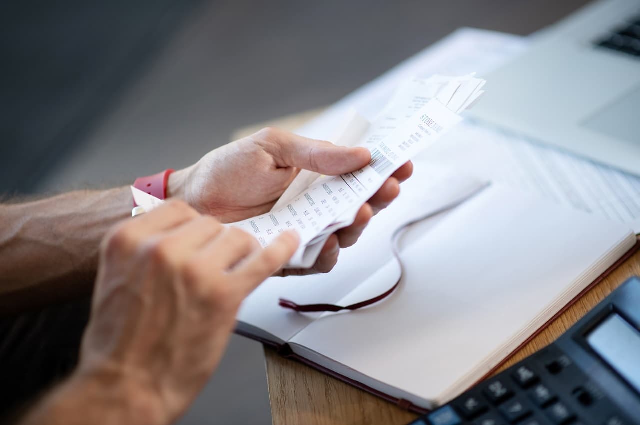 Pessoa (seu rosto não aparece na imagem) segurando notas fiscais e papéis para declarar empréstimo no imposto de renda.