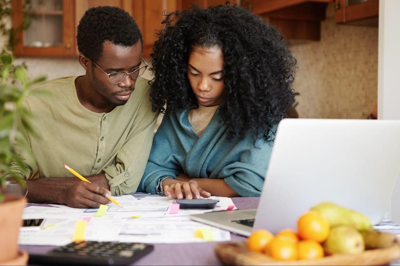 Casal com expressões concentradas declarando saque FGTS no imposto de renda. O homem analisa contas com um lápis, enquanto a mulher utiliza a calculadora.