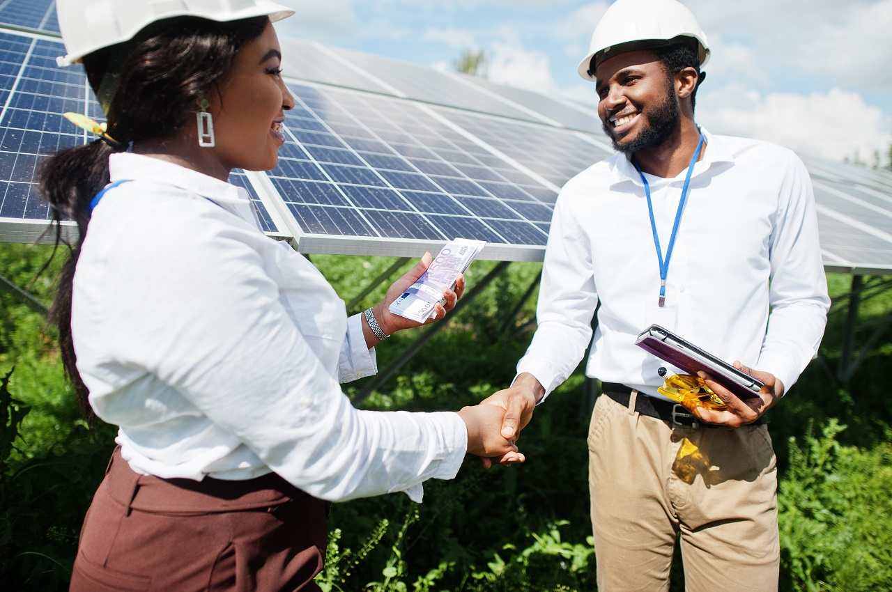 Mulher e homem sorridentes dando um aperto de mão no trabalho. Eles vestem equipamentos de proteção para manutenção de placas solares.