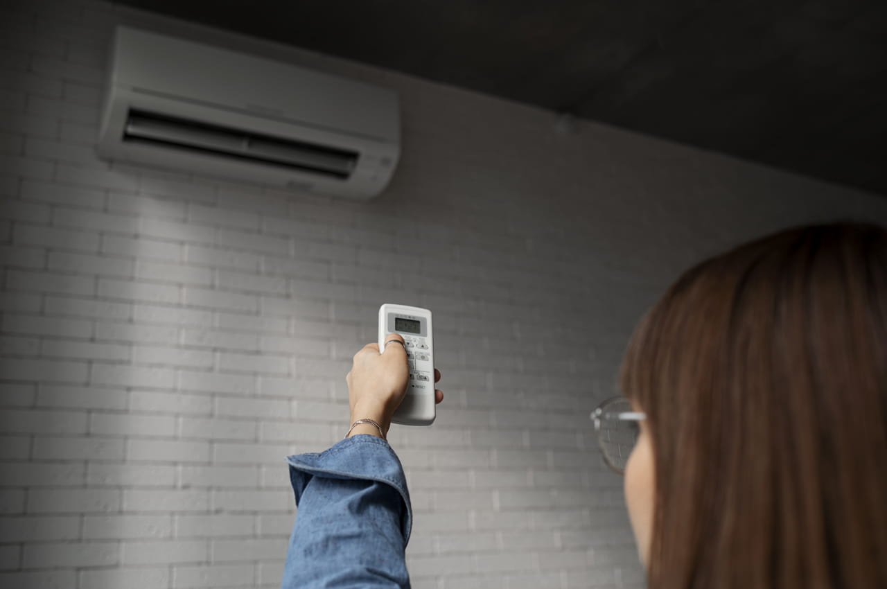 Mulher de cabelos castanhos e óculos de grau aponta controle de ar condicionado para o aparelho para economizar energia.