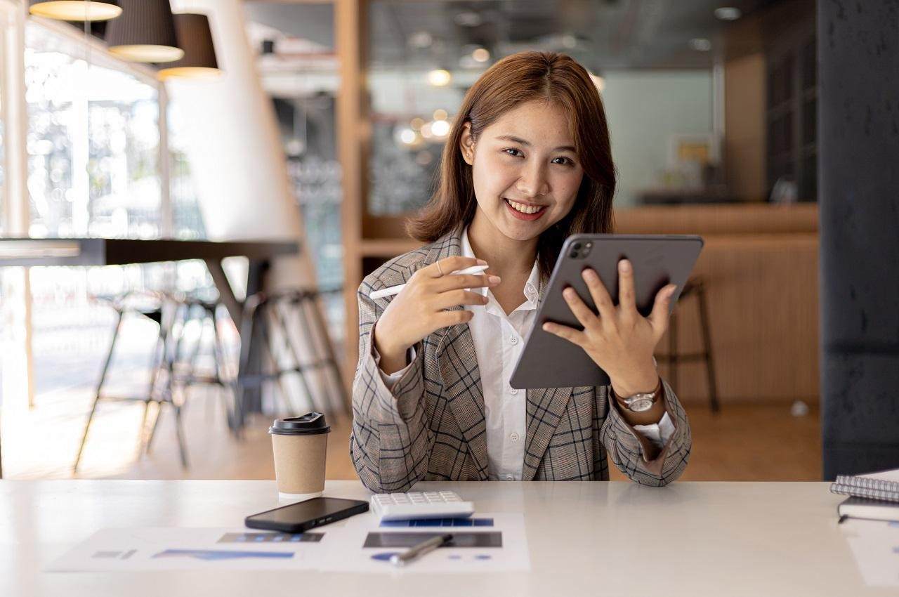 A imagem mostra uma mulher sentada, sorridente e usando seu tablet.