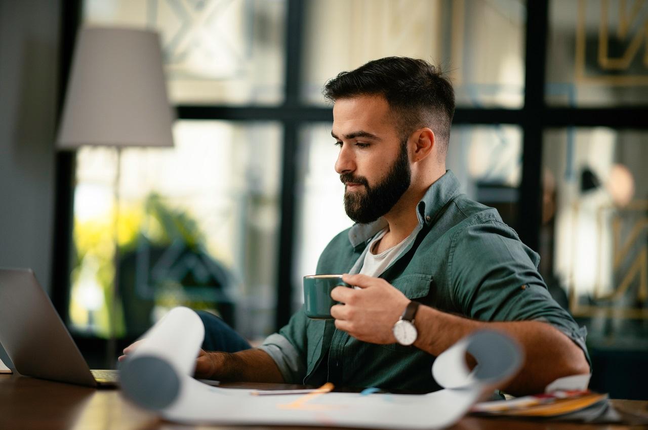 A imagem mostra um homem tomando um café e usando seu laptop.