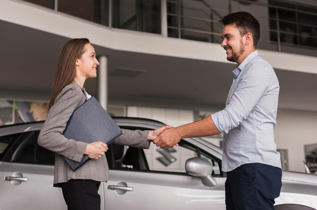 Mulher cumprimentando um homem com um aperto de mão, em sinal de haverem feito um financiamento de carro seminovo.