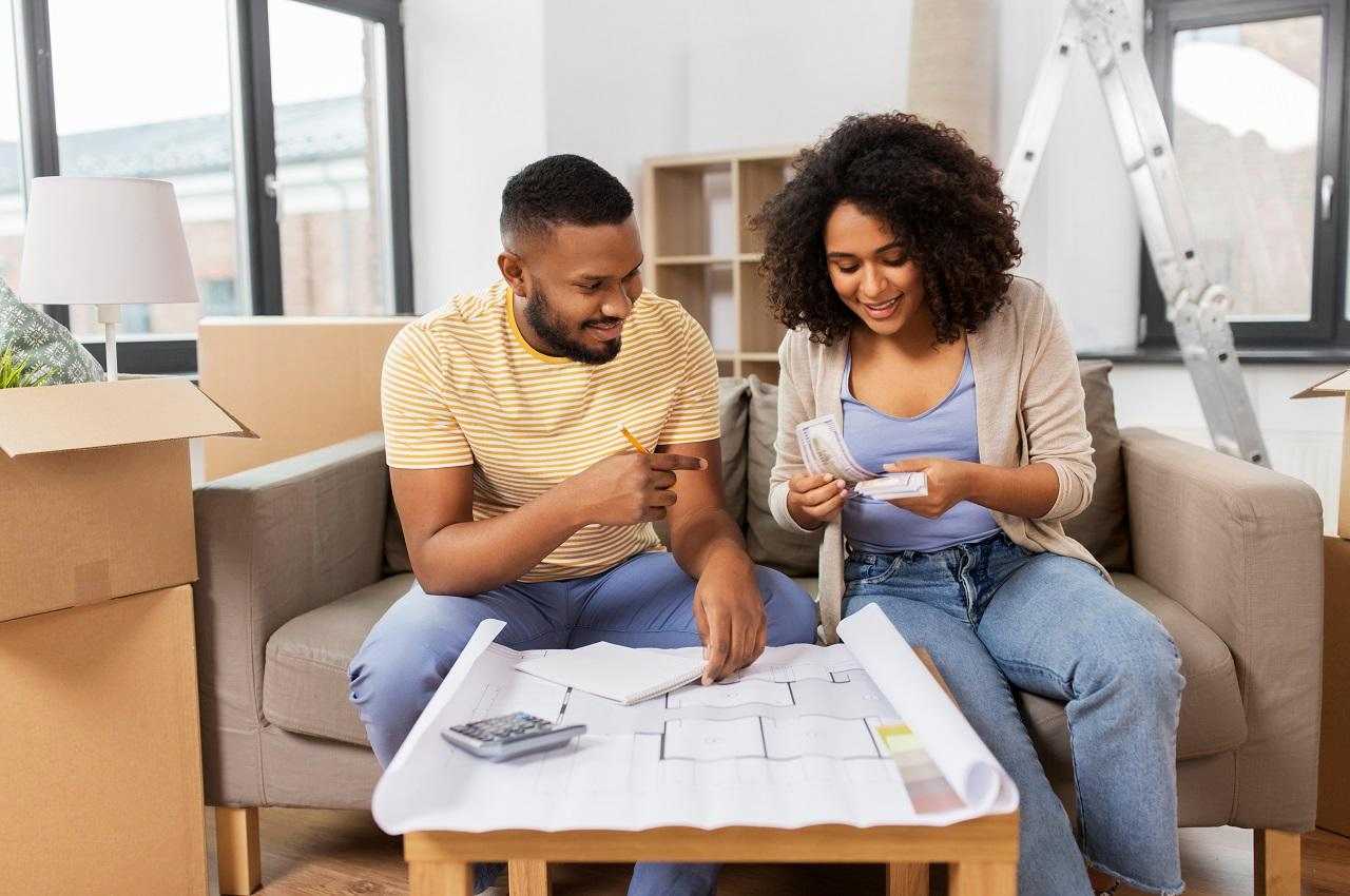 Homem e mulher sentados no sofá de uma sala de estar analisando a planta de arquitetura do imóvel.