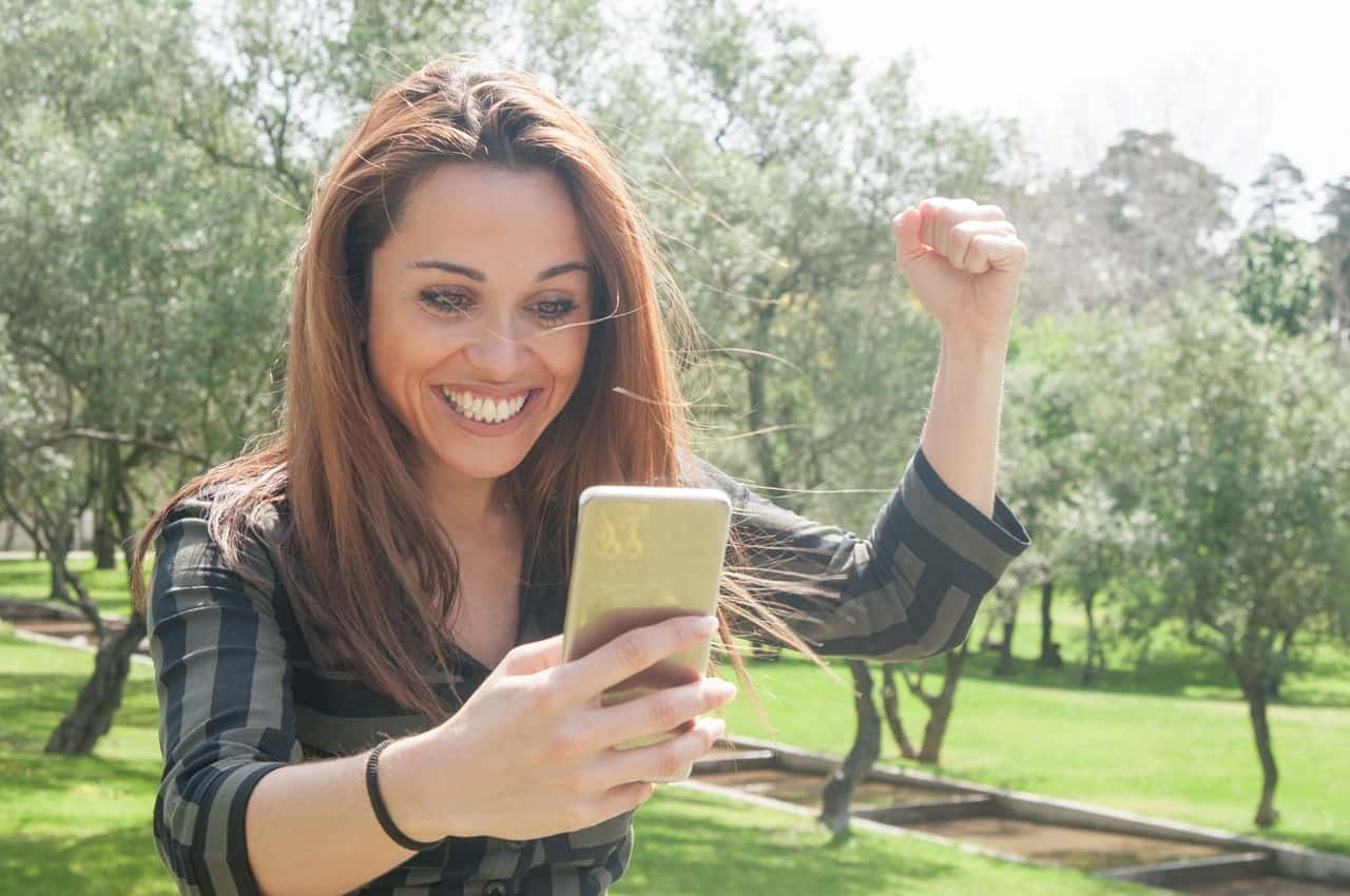 Mulher com expressão sorridente, as mãos levantadas e segurando um celular comemorando simulação de financiamento de veículos.