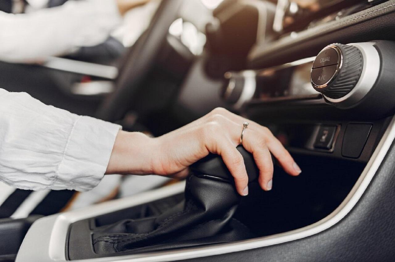 Pessoa dirigindo carro híbrido segurando o câmbio do carro e o volante