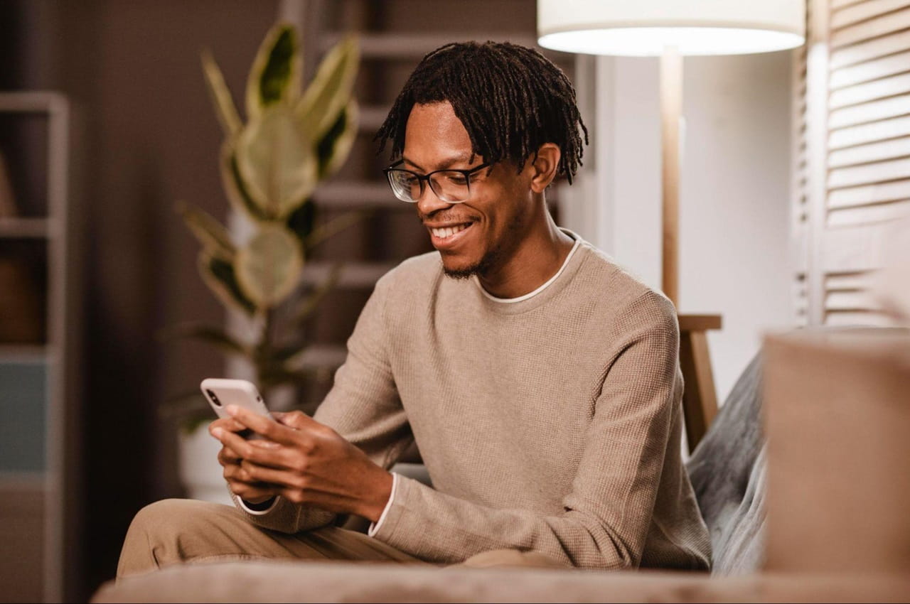 Homem sorridente usa óculos e um celular para descobrir saber quanto custa para renovar CNH.