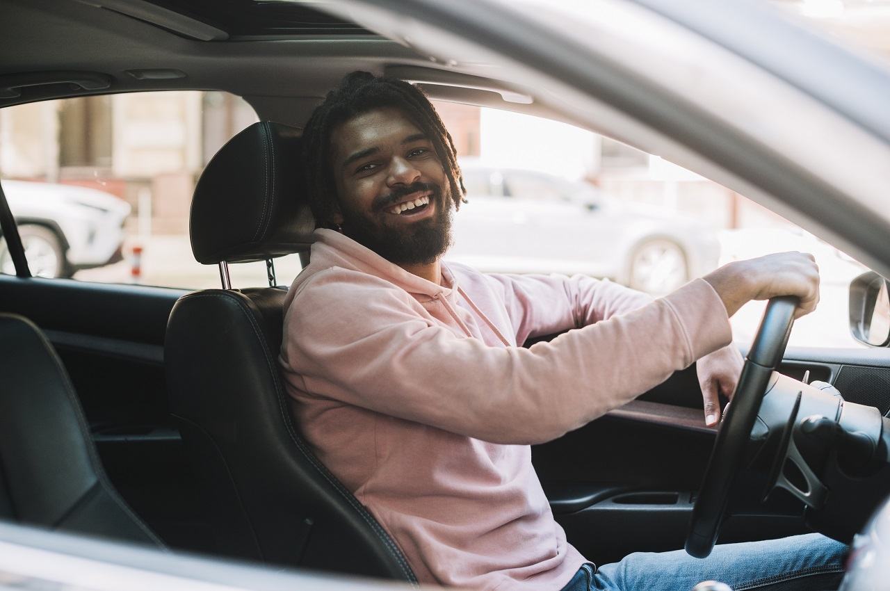 Homem negro sorridente, vestindo blusa social rosa e dirigindo veículo com freio ABS.