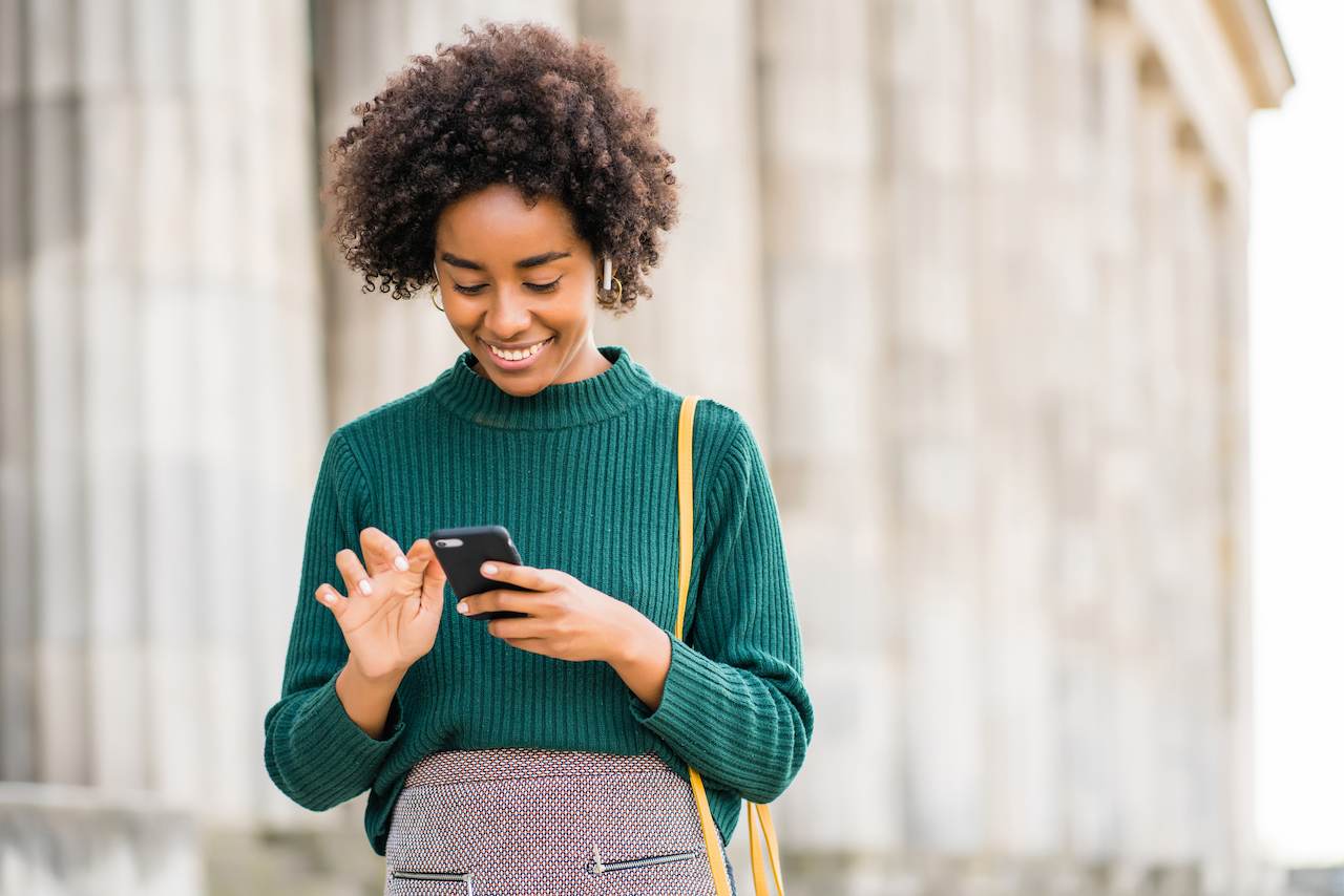 A imagem mostra uma mulher sorridente, usando seu celular. 