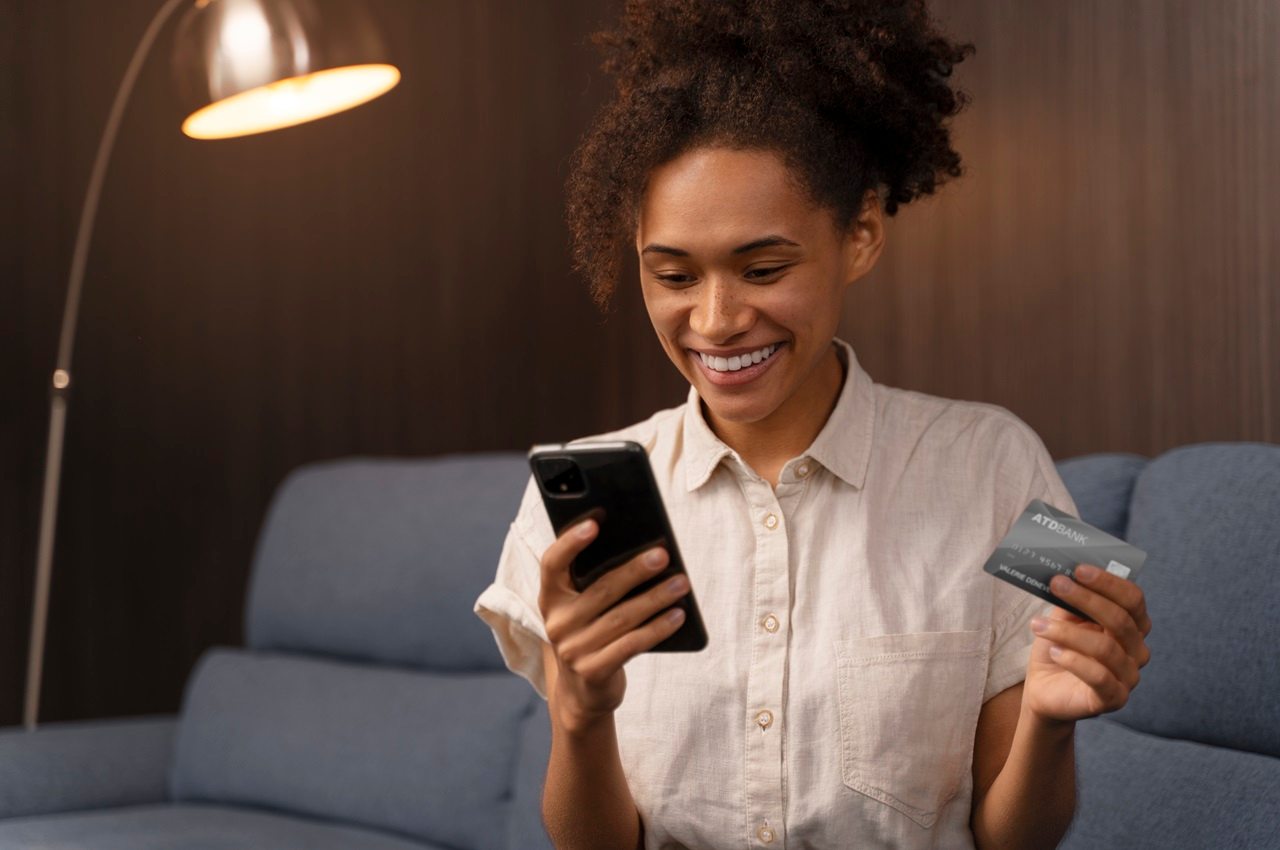 A imagem mostra uma mulher sorridente, usando seu celular para pagar contas com o cartão de crédito.