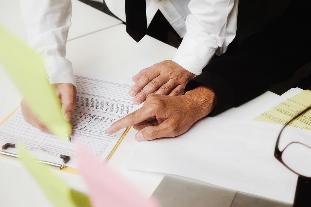 Pessoas lendo e analisando um contrato de alienação fiduciária de veículo que está em cima de uma mesa.