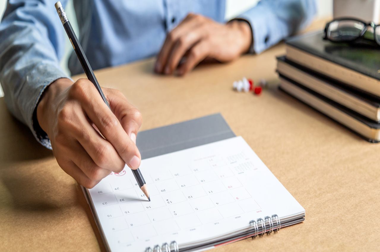 Pessoa (o rosto não aparece na imagem) anotando um dia no calendário para pagar contas de início do ano.