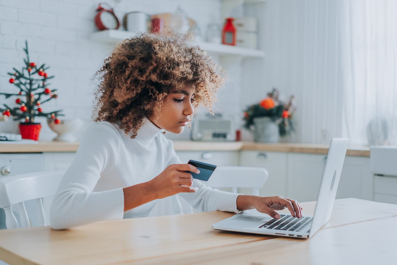 A imagem mostra uma mulher usando seu laptop para realizar uma compra no cartão de crédito.