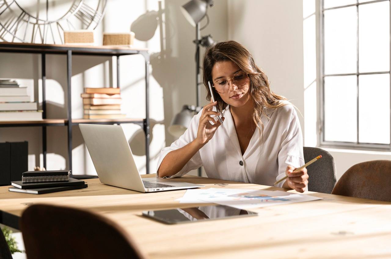 Mulher de cabelos castanhos e com expressão concentrada. Ela no escritório e realizando anotações no trabalho.