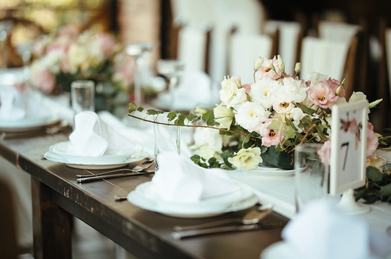 Foco em mesa de casamento para festa de casamento com pratos enfeitados por guardanapos e arranjos florais.