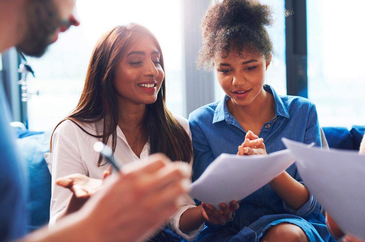 Mulheres com expressões sorridentes analisando contrato de consórcio ou financiamento ao lado de um vendedor no escritório.