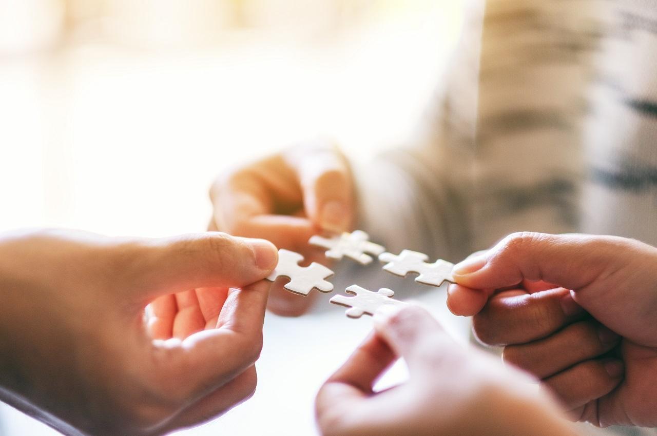 Mãos segurando quatro peças de um quebra-cabeça e aproximando as peças umas das outras.