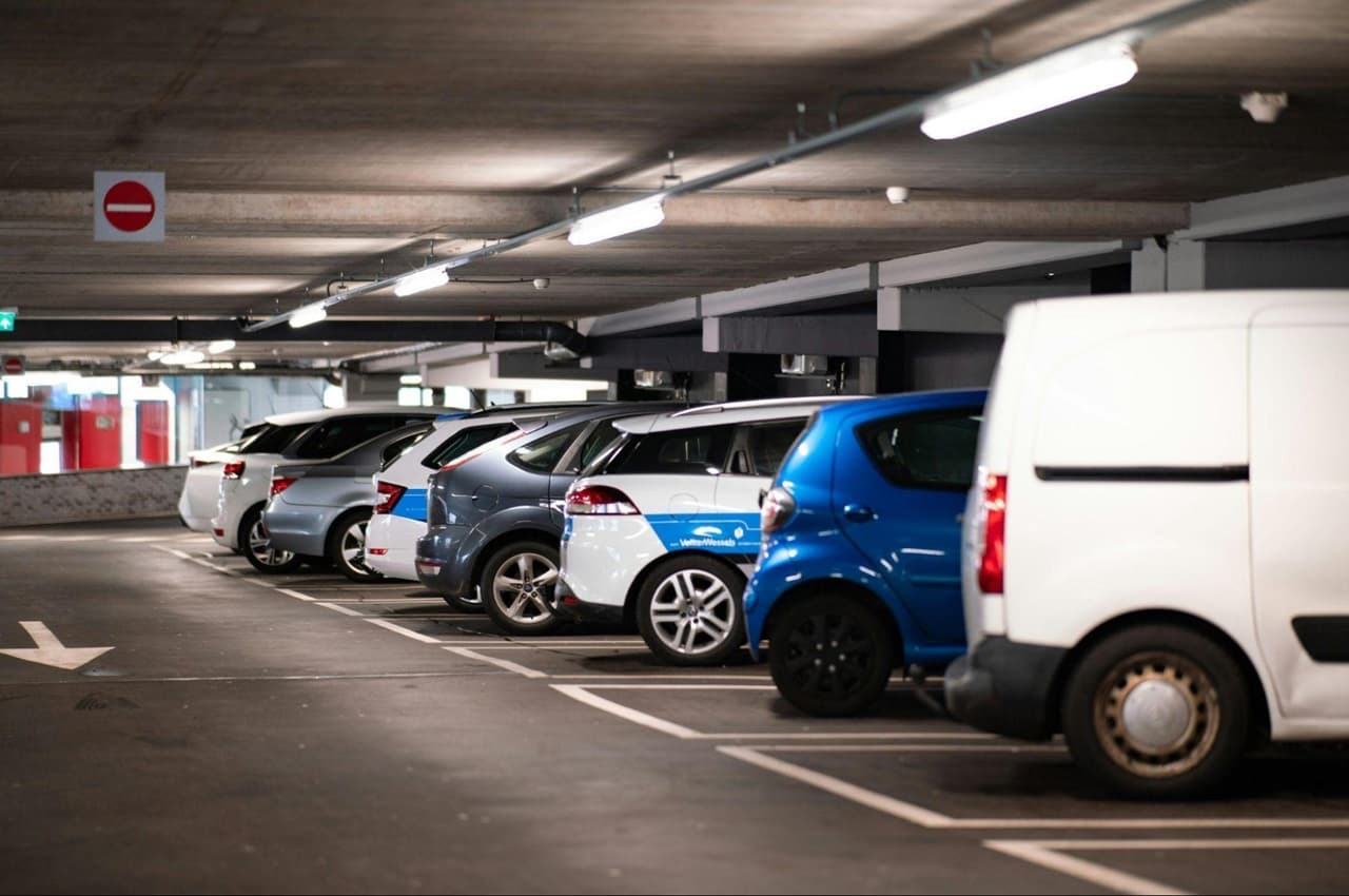 Estacionamento subterrâneo com veículos e mini van branca estacionados.