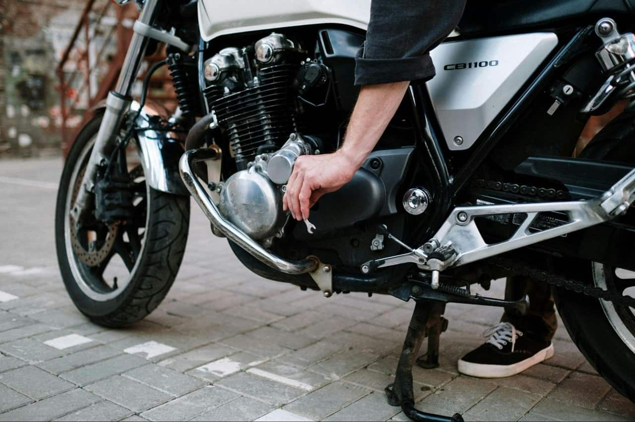 Mão masculina ajustando pedal de moto preta com chave de fenda.