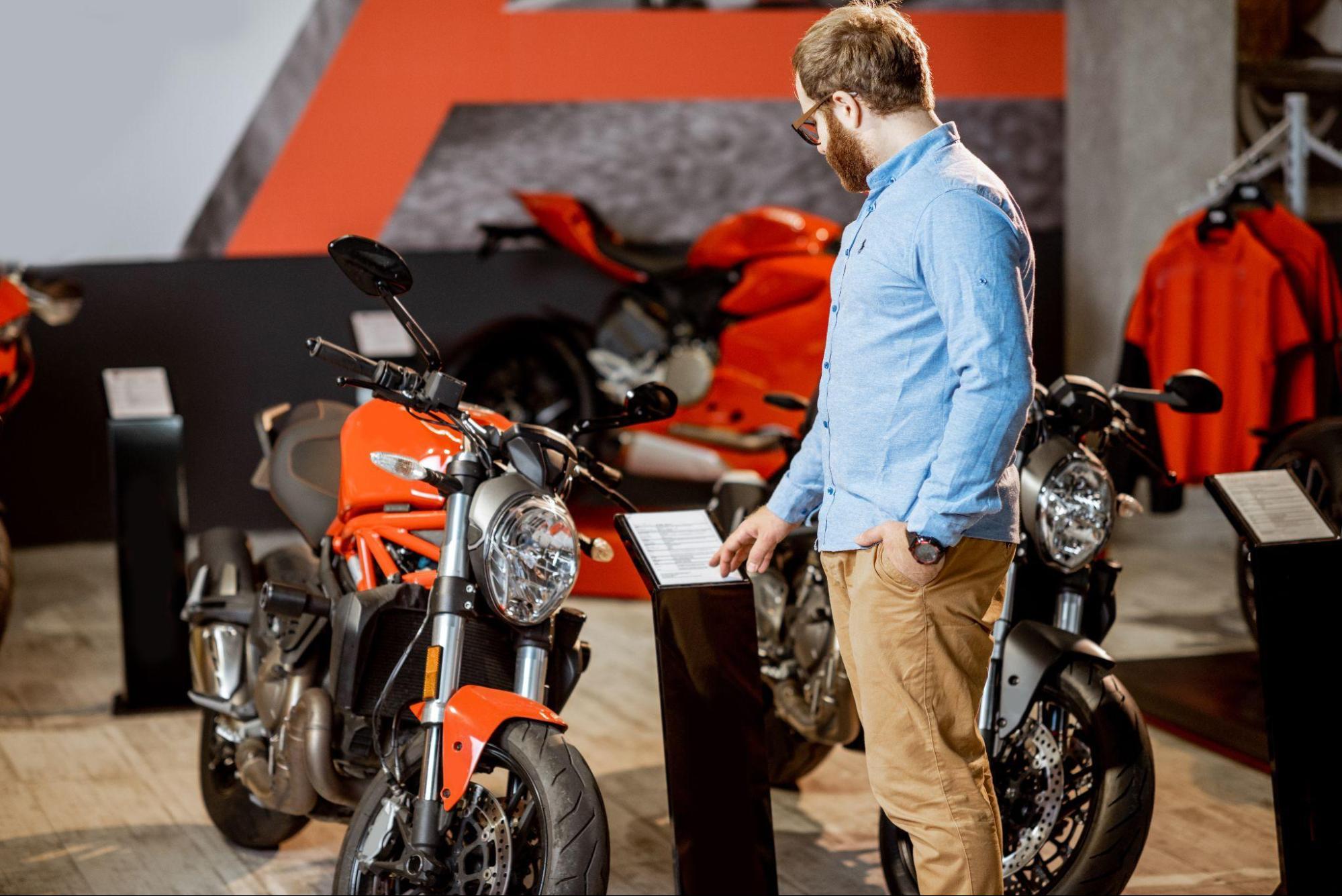 Homem examinando uma motocicleta vermelha em uma concessionária e entendendo como funciona o financiamento de moto.