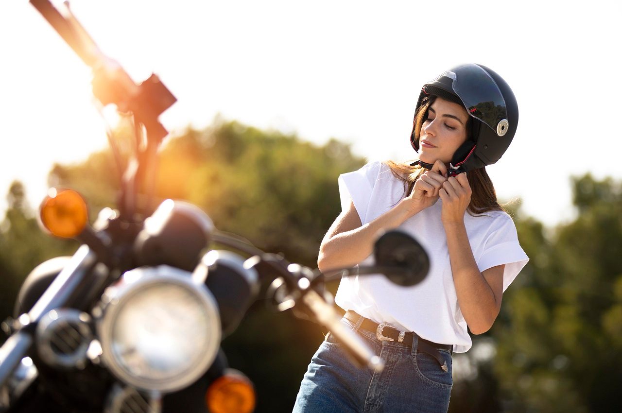 A imagem mostra uma mulher, ao lado de sua moto, vestindo seu capacete.