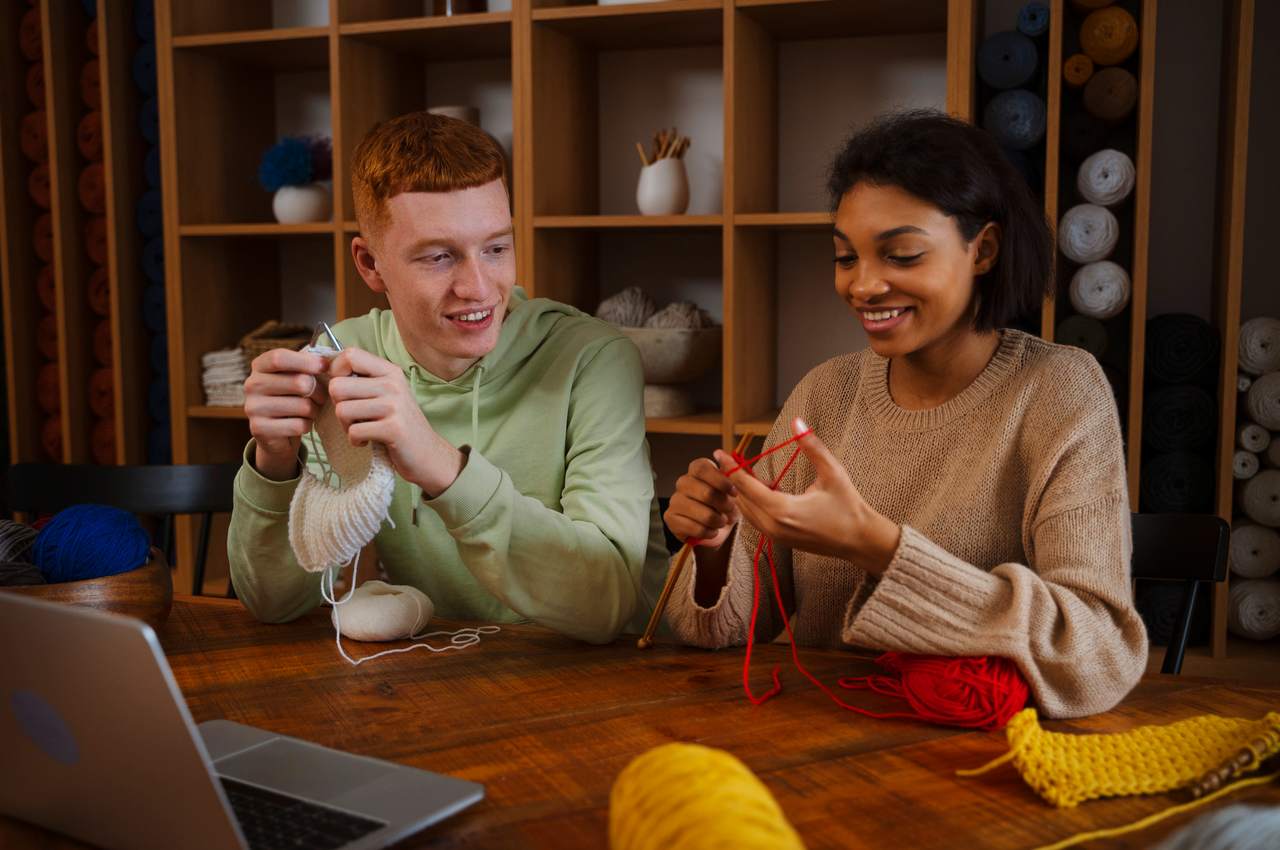 Duas pessoas sorridentes utilizando agulhas de crochê e lã para bordar como hobbie que dá dinheiro.