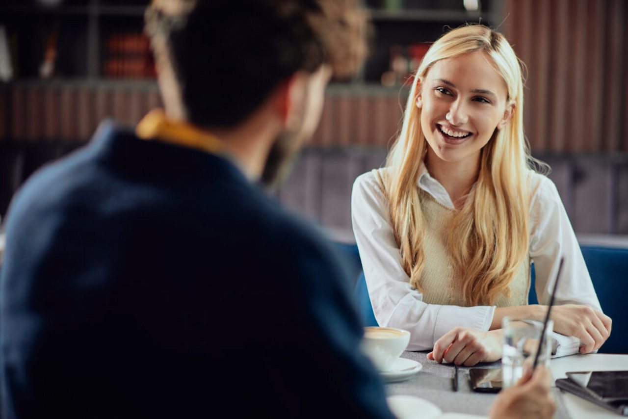 A imagem mostra um homem e uma mulher em reunião de negócios. Ambos estão sorridentes.