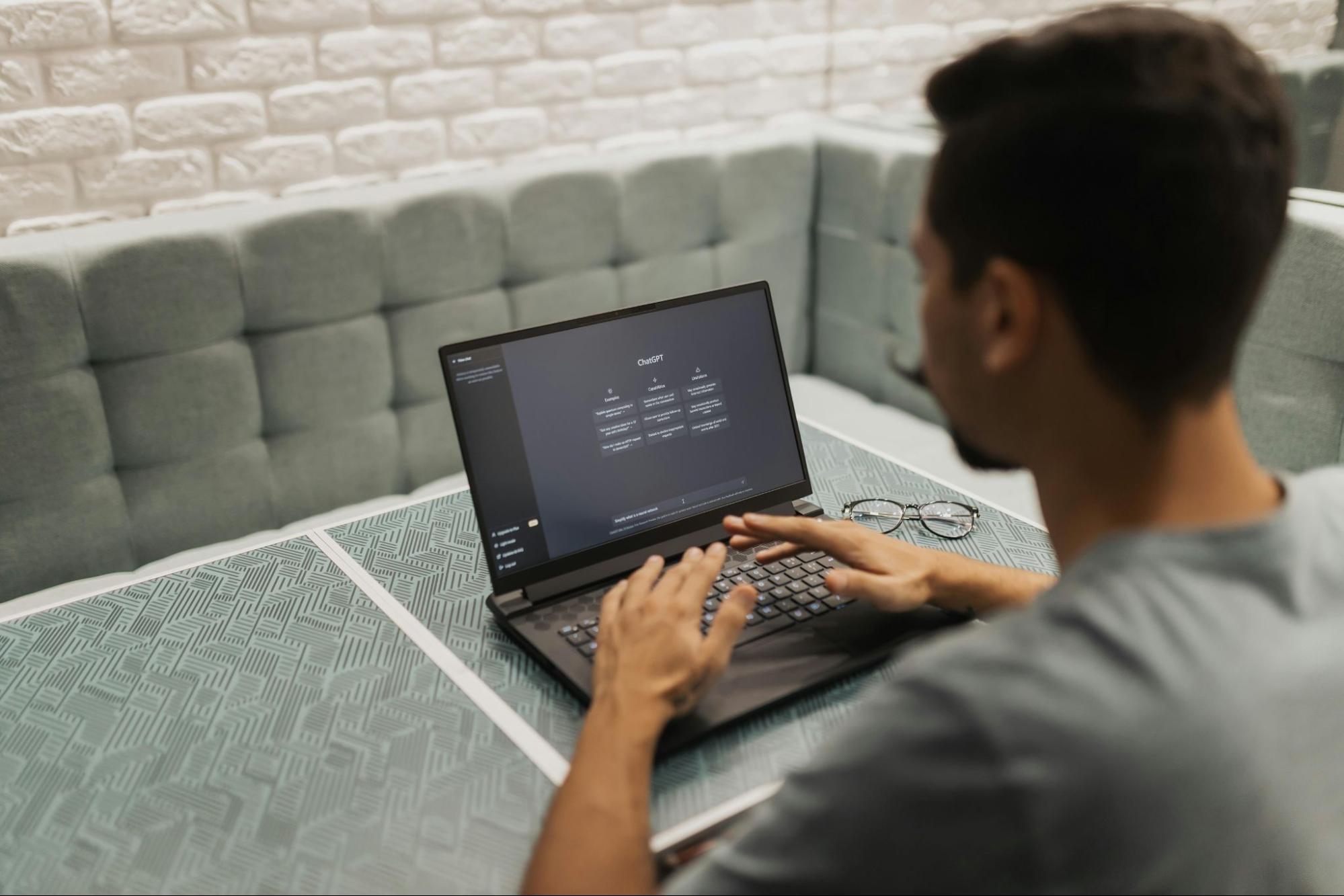 Um homem usando camiseta cinza em uma sala de reunião, também na cor cinza. Ele está usando seu laptop.