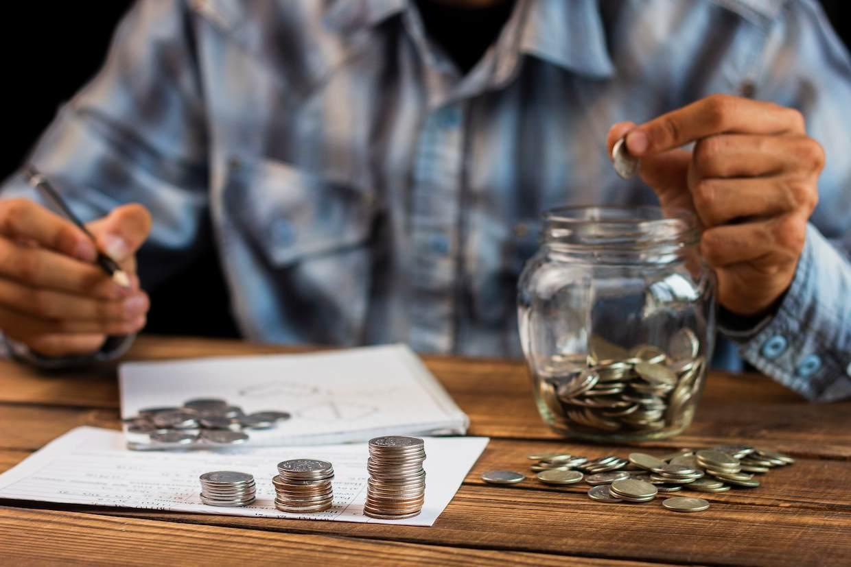 Um homem analisando suas finanças com um pote de moedas e uma planilha de controle, a fim de se prevenir de golpes de empréstimo.