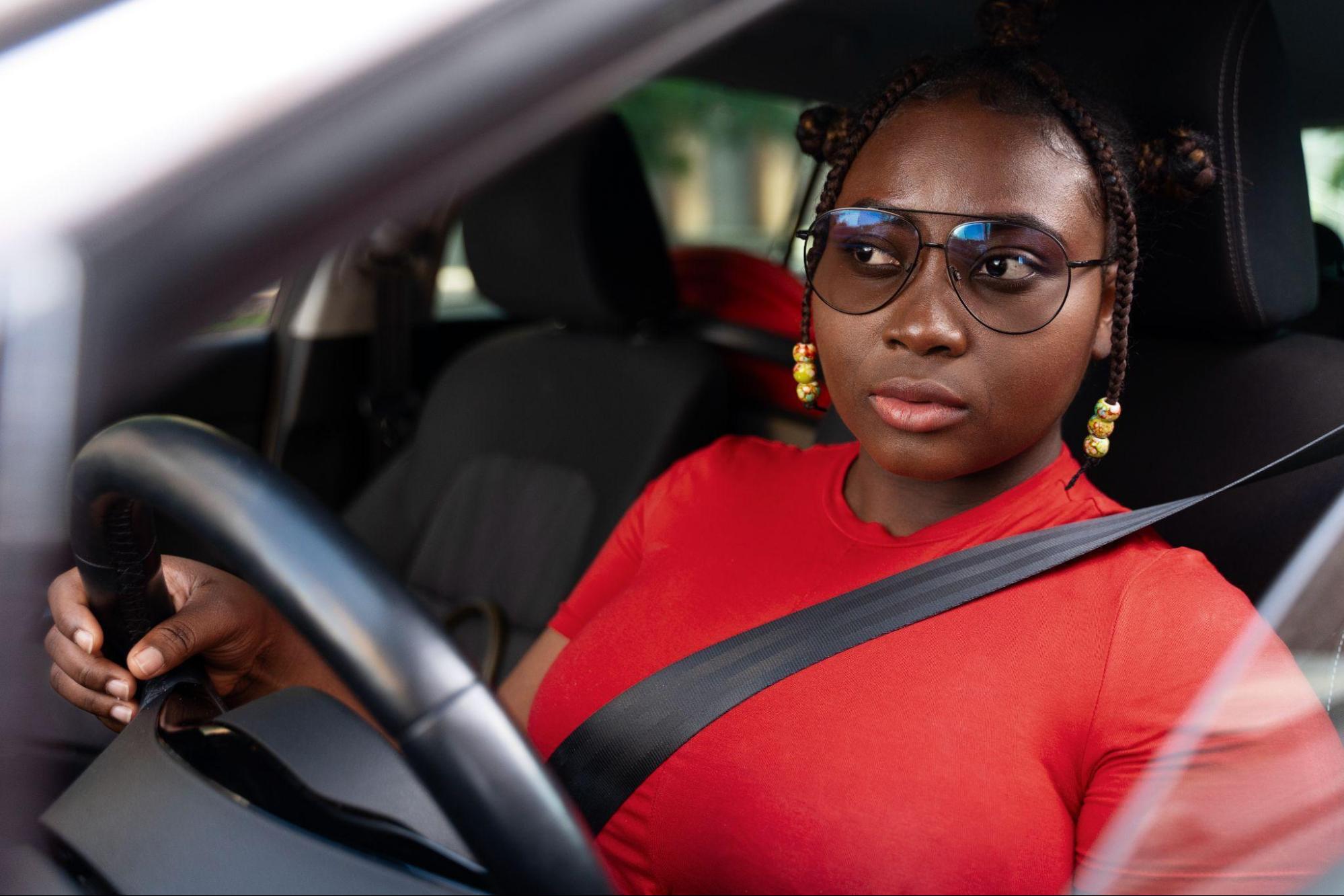 Mulher usando camiseta vermelha e óculos escuros dirigindo seu carro.