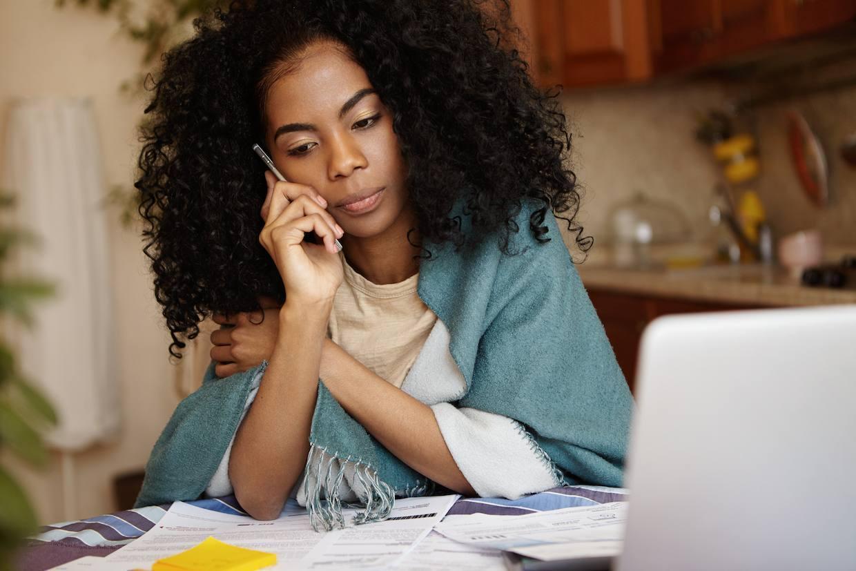 Mulher conversando no celular enquanto organiza documentos e lida com dívidas do cartão de crédito do falecido.