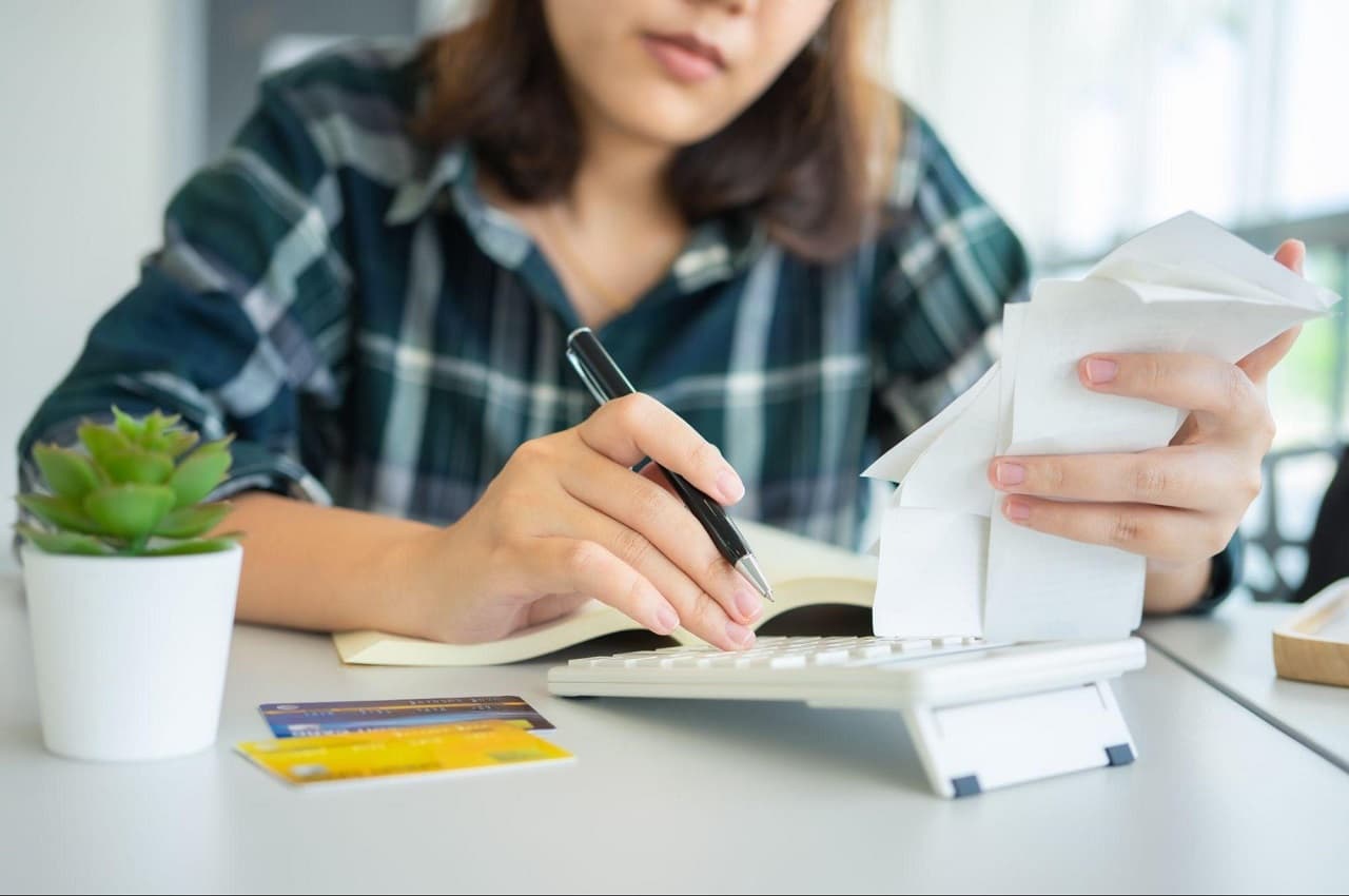 Mulher com expressão concentrada segurando com as mãos papéis para análise de empréstimo pessoal e utilizando calculadora.