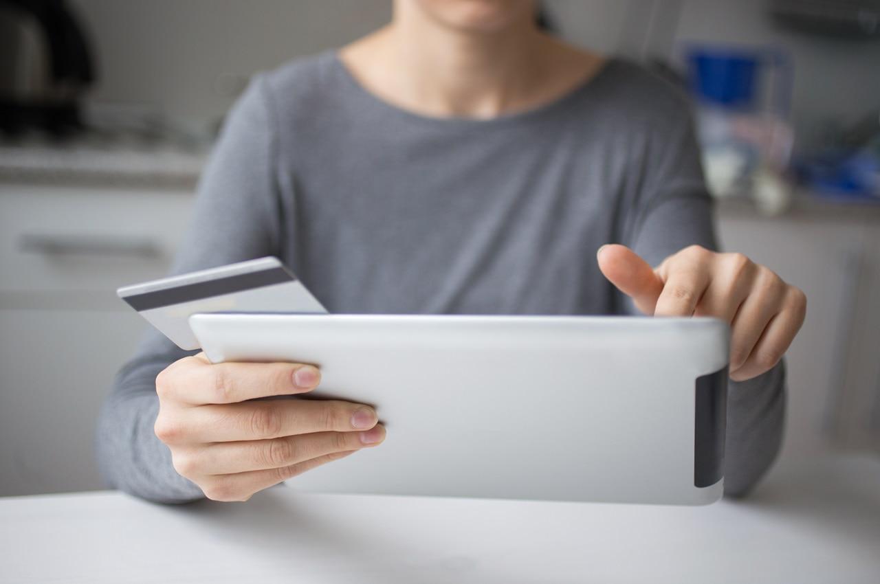 Pessoa mexendo em um tablet e segurando um cartão de crédito. Ela está pesquisando sobre como reduzir parcela de empréstimo pessoal.