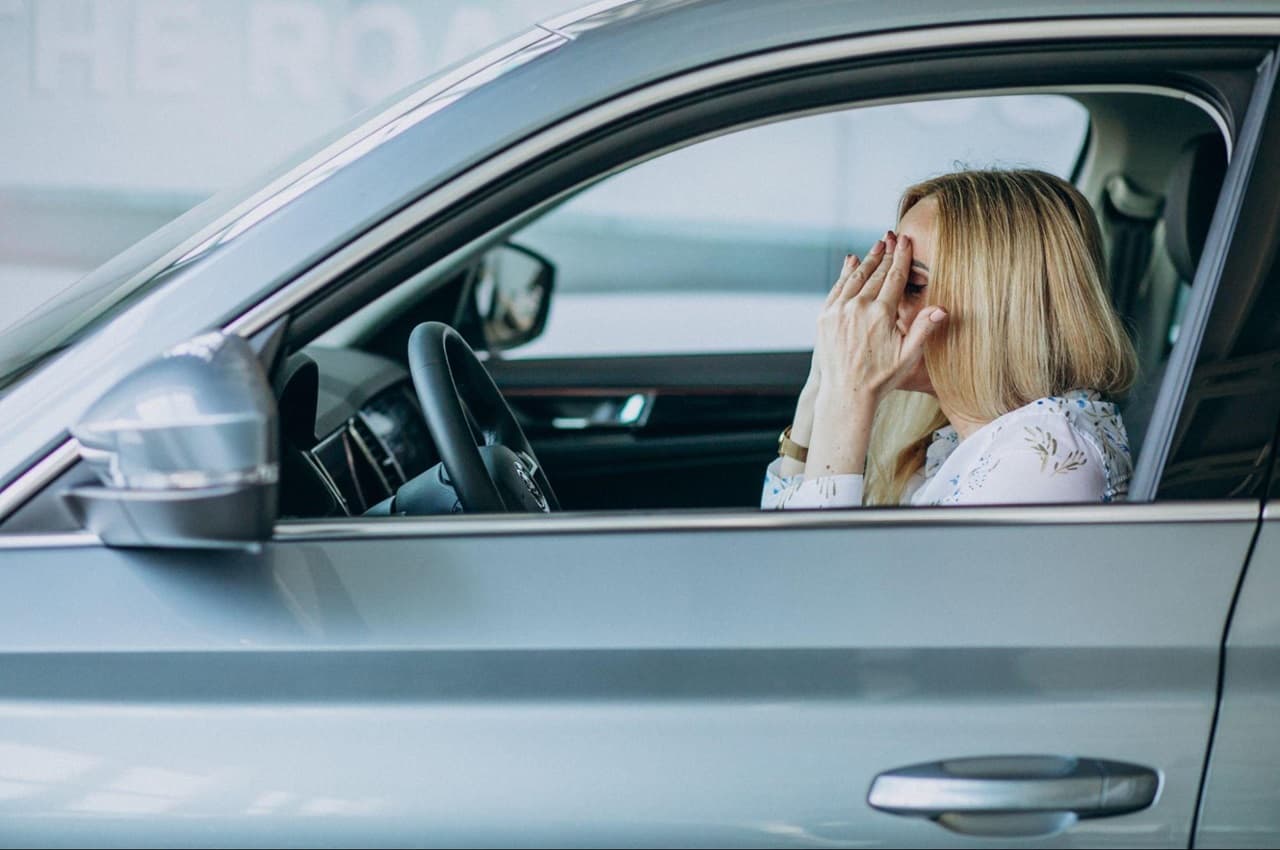 Mulher sentada em banco de motorista de carro apoiando o rosto com as duas mãos após a CNH ser cancelada.